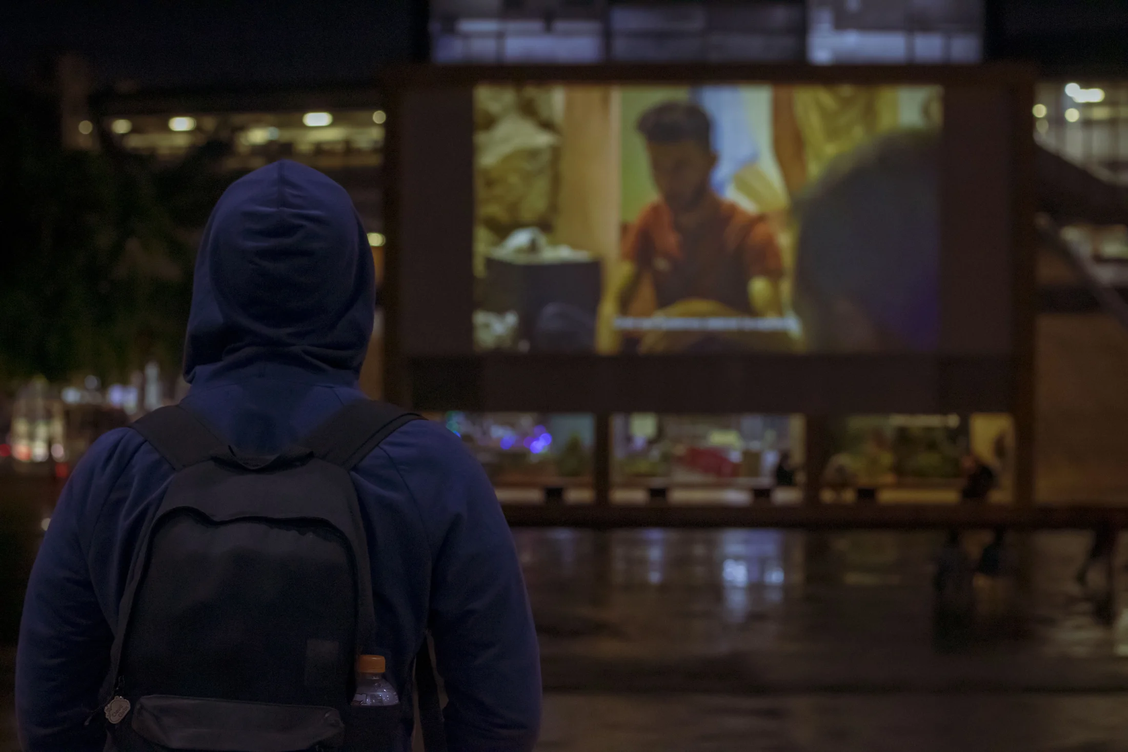Una persona mira una película proyectada al aire libre en el barrio.