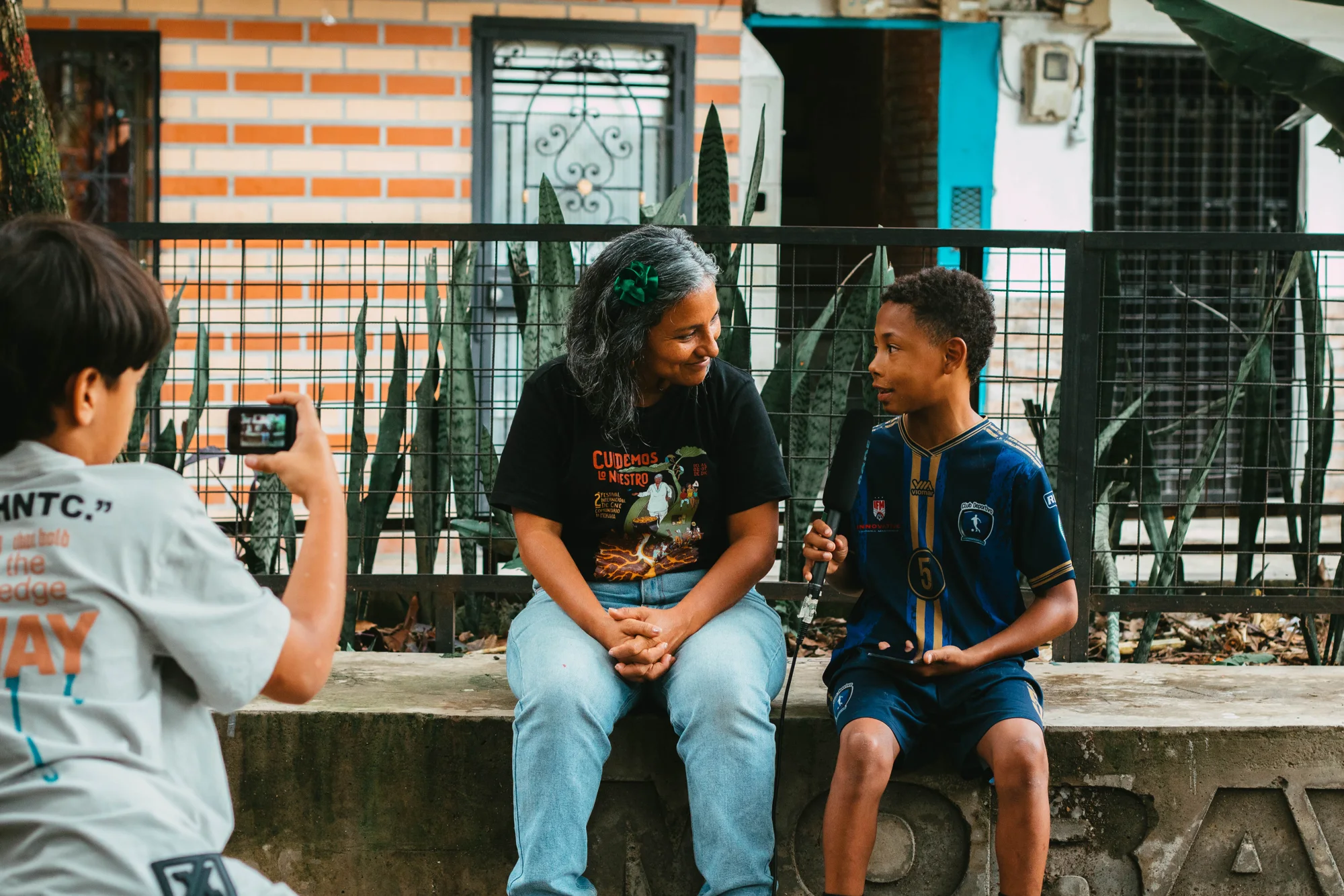 Una persona graba con una cámara una entrevista entre un niño y una mujer en el barrio